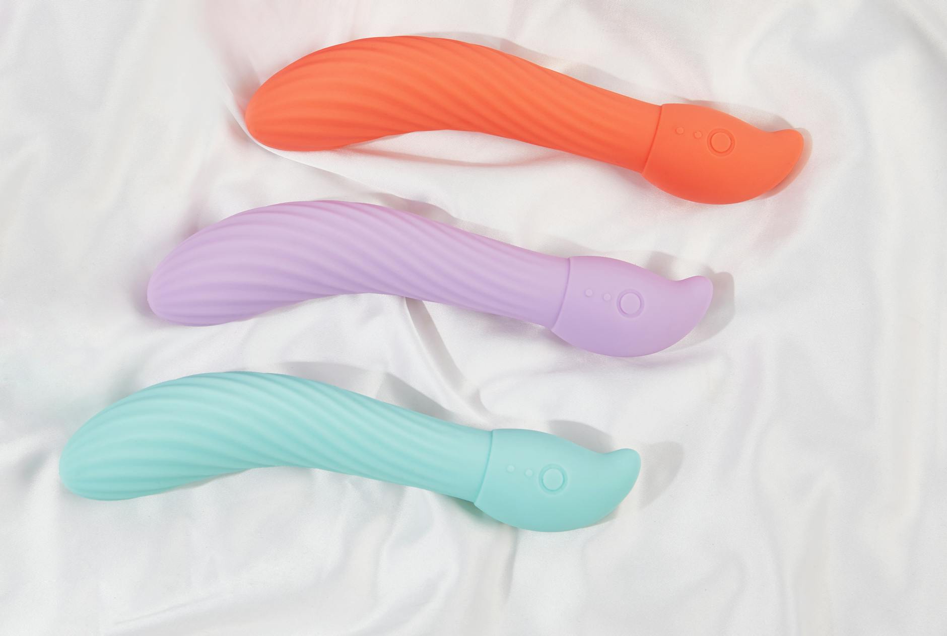 Photo of three colorful vibrators arranged on white fabric highlighting smooth texture