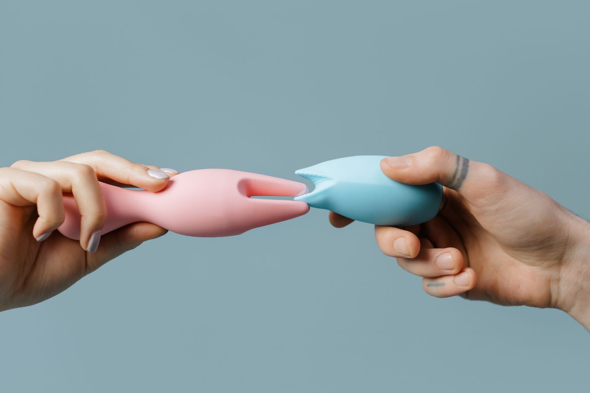 Hands holding pastel silicone vibrators against a soft background.