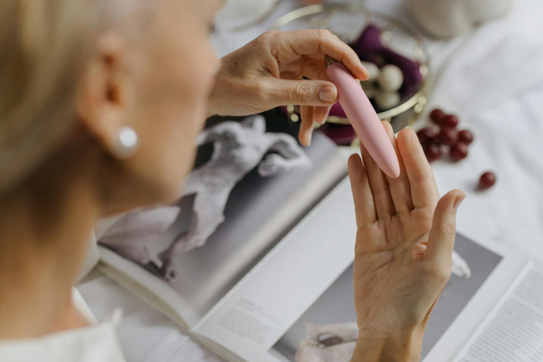 Woman holding a personal vibrator with art books nearby, emphasizing intimate self-discovery