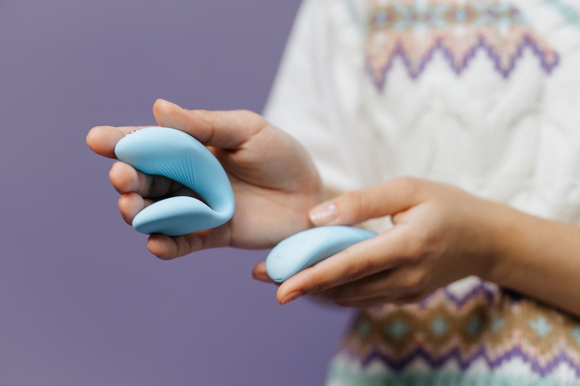 Manos sosteniendo un vibrador azul elegante contra un fondo púrpura