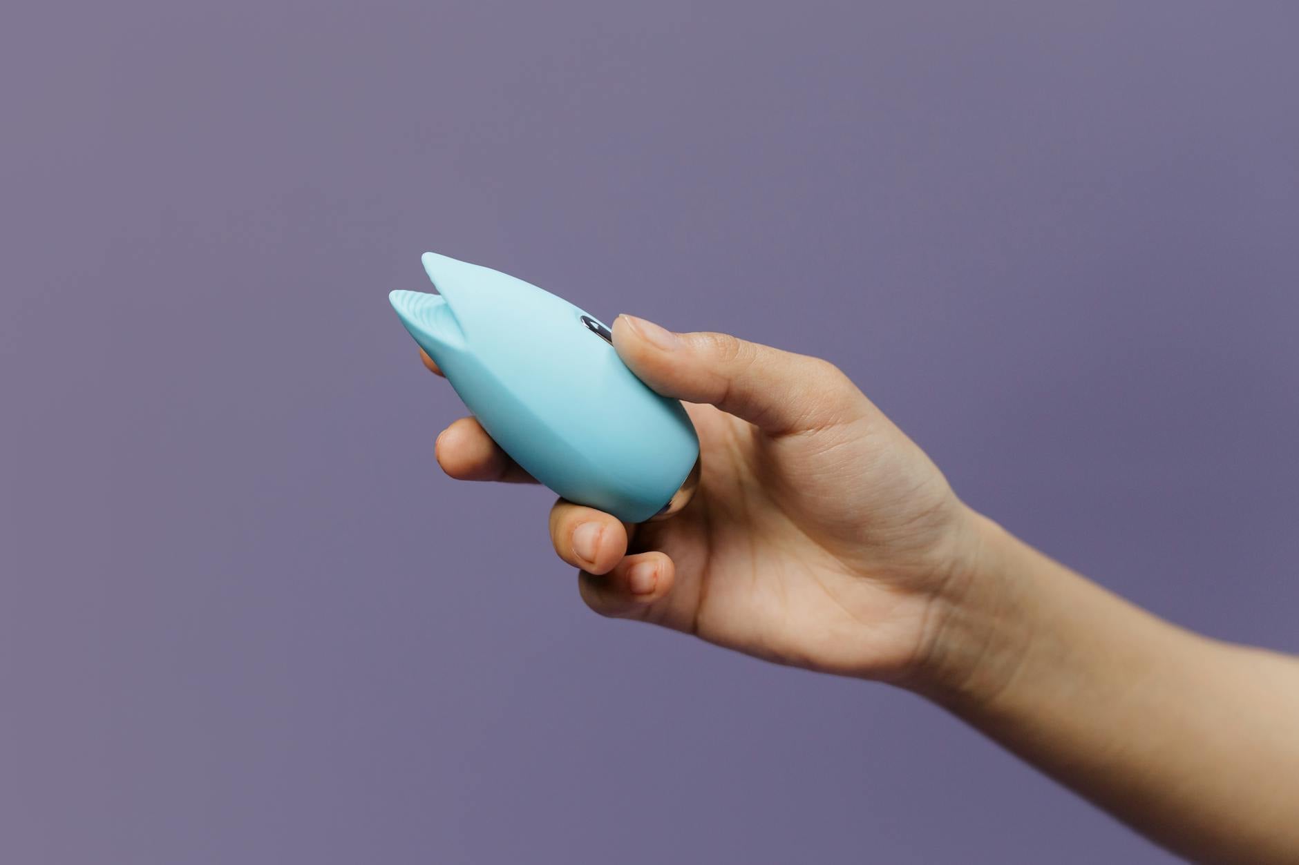 A blue silicone vibrator held against a solid purple background, representing self-love and sexual pleasure.