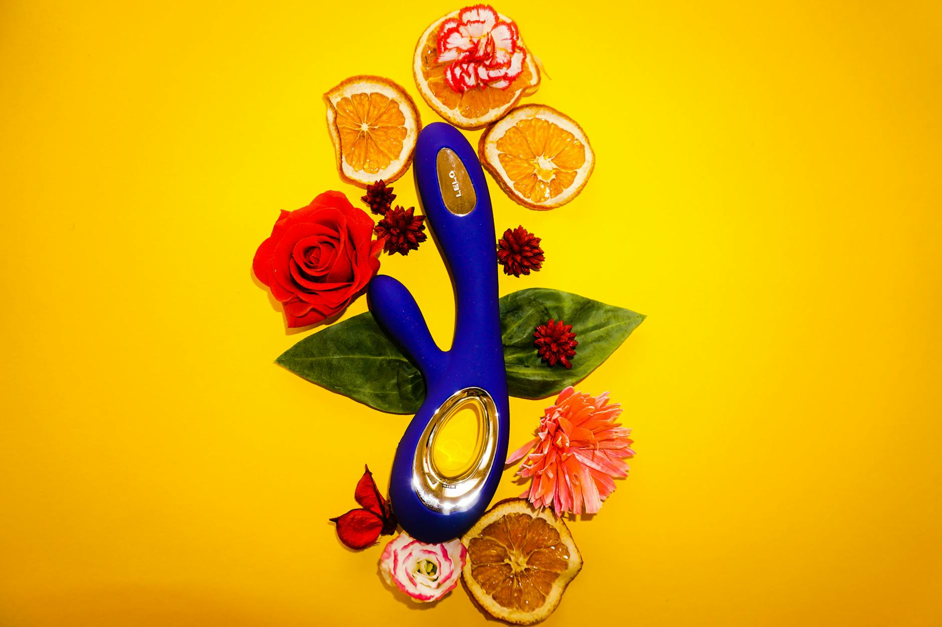 Bright lemon-colored vibrator surrounded by fresh lemons and citrus elements on a vibrant yellow background