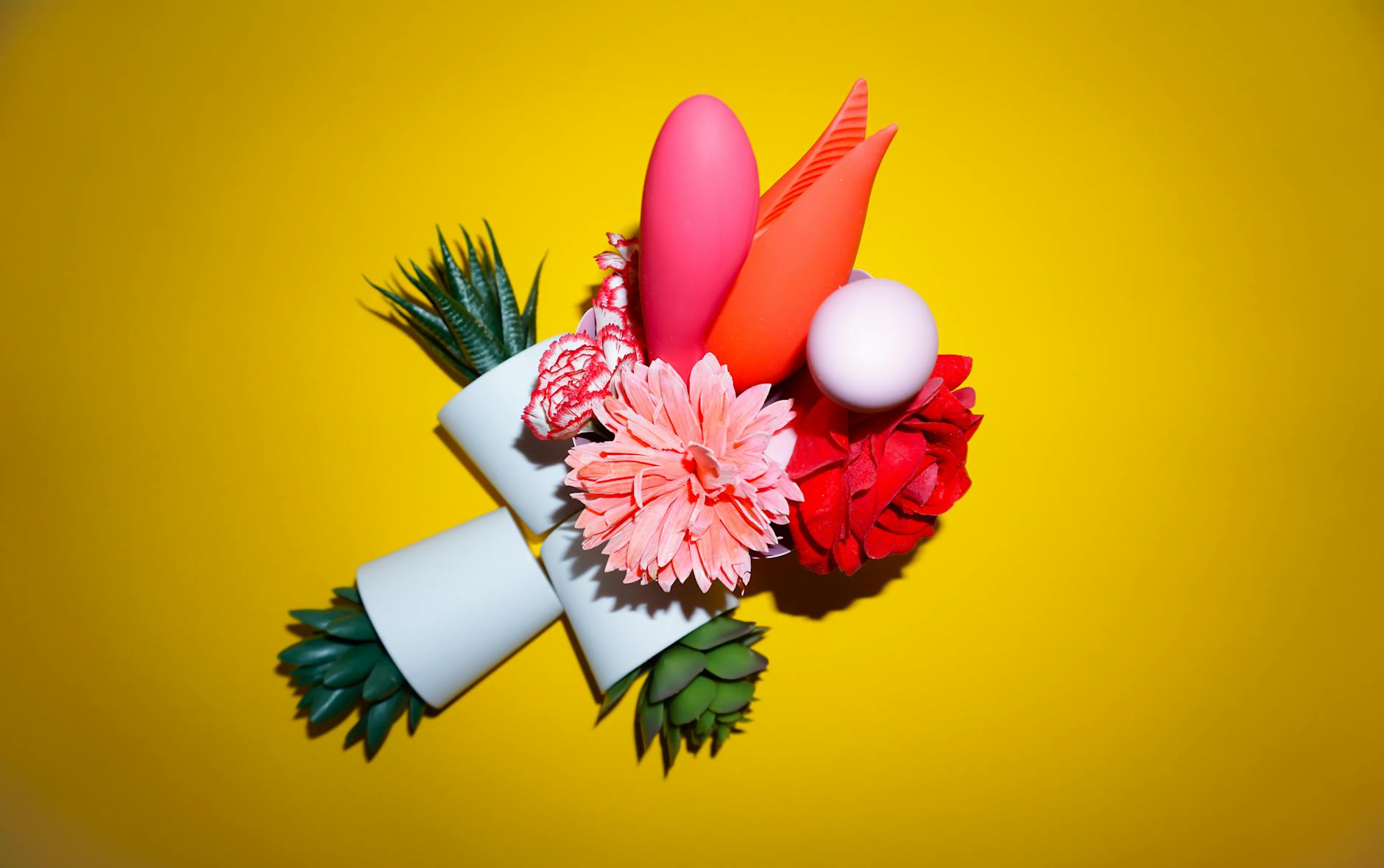 Two hands holding pink and blue silicone clitoral vibrators against a pastel background
