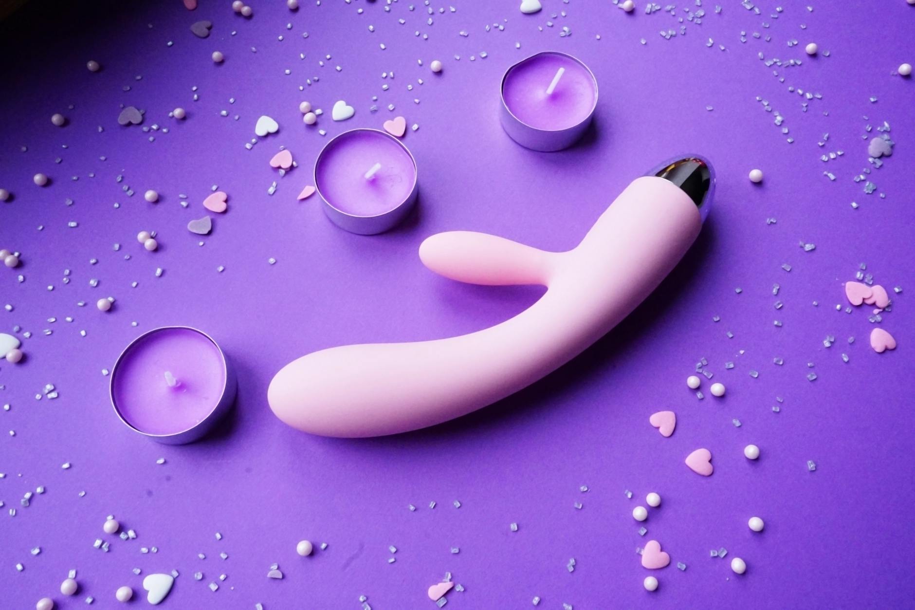 Pink vibrator on purple background with heart confetti and candles for romantic intimacy